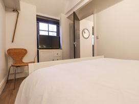 A bedroom with a bed a wicker chair a cabinet with a television and an open door at Bee Cottage Ottinge near Lyminge