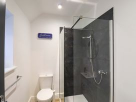 A bathroom with a toilet and a glass shower enclosure with dark tiles at Bee Cottage in Ottinge near Lyminge