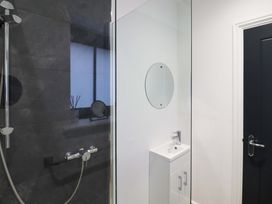 A bathroom with a shower area a small sink with cabinet and an oval mirror at Bee Cottage in Ottinge near Lyminge