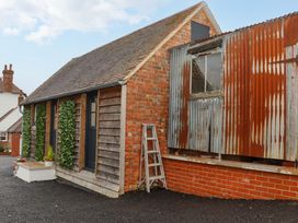 A small brick and wood building with a corrugated metal section and a ladder outside at Bee Cottage in Ottinge near Lyminge