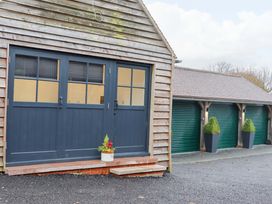 A wooden building with blue double doors and a potted plant next to a row of green garage doors with topiary plants in tall black pots at Bee Cottage Ottinge near Lyminge