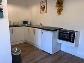 A kitchen with white cabinets a microwave a toaster a kettle a small fridge a sink and a small oven with stove at Bee Cottage in Ottinge near Lyminge
