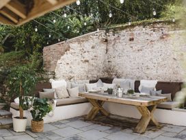 An outdoor area with a wooden table and cushioned bench at Lower Well Farm House in Totnes