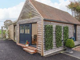 A small wooden building with a double door open showing a table and chairs inside and plants on the exterior walls at Kingfisher Cottage in Ottinge near Lyminge