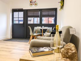 A dining area with a table set for four near black double doors and a beige sofa with a book bottle and glasses at Kingfisher Cottage in Ottinge near Lyminge