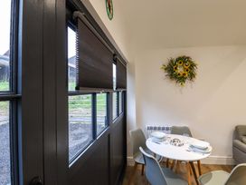 A dining area with a round white table set with bowls and glasses surrounded by four chairs and a floral wreath on the wall at Kingfisher Cottage in Ottinge near Lyminge