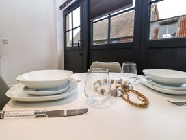 A dining table set with plates bowls glasses and cutlery near black framed windows at Kingfisher Cottage in Ottinge near Lyminge