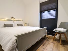 A bedroom with a bed with white bedding and gray pillows fairy lights on the headboard a gray chair with folded towels and a black door at Kingfisher Cottage in Ottinge near Lyminge