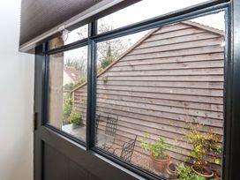 A view of a wooden shed wall and a small patio with metal chairs and potted plants from inside a room at Kingfisher Cottage Ottinge near Lyminge