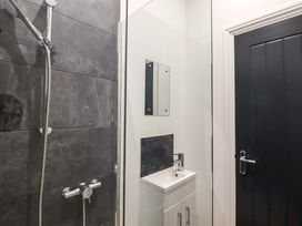 A bathroom with a shower area with dark tiles a small white sink with a mirror above and a black door Kingfisher Cottage Ottinge near Lyminge
