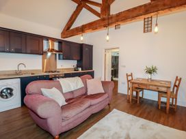 A living room with a pink sofa and wooden dining table with two chairs and kitchen cabinets at The Old Parlour in Cwm near Dyserth