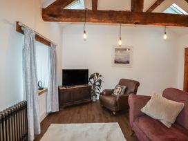 A living room with a TV on a wooden cabinet a brown armchair a purple sofa with cushions and curtains on the window at The Old Parlour in Cwm near Dyserth