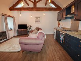 An open plan living room and kitchen with exposed wooden beams a sofa a rug a television and dark kitchen cabinets at The Old Parlour in Cwm near Dyserth