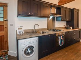 A kitchen with dark cabinets a washing machine a sink and a gas stove at The Old Parlour in Cwm near Dyserth