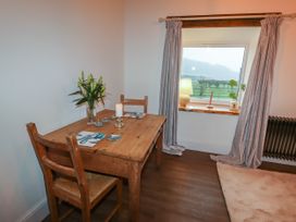 A dining room with a wooden table and chairs next to a window with curtains and a table lamp at The Old Parlour in Cwm near Dyserth