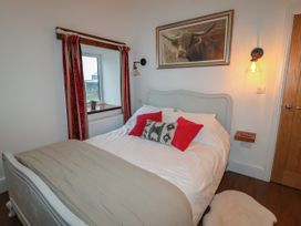A bedroom with a bed with pillows a window with red curtains a framed painting and a small wooden shelf at The Old Parlour in Cwm near Dyserth