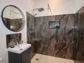 A bathroom with a sink and a round mirror next to a walk-in shower with dark marble walls at The Old Parlour in Cwm near Dyserth