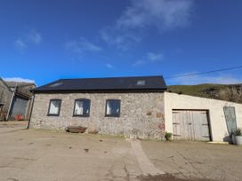 A stone building with three windows and a wooden door next to an open concrete area at The Old Parlour in Cwm near Dyserth