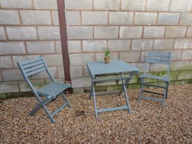 A small outdoor seating area with two chairs and a square table with a potted plant on top against a brick wall at The Old Parlour in Cwm near Dyserth