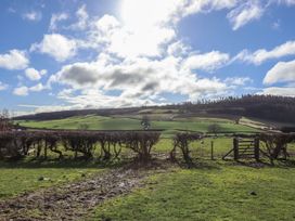 A grassy field with a hedge and a wooden gate and hills in the background at The Old Parlour in Cwm near Dyserth