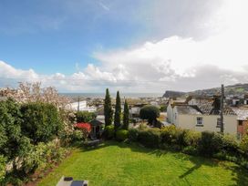 A garden with green grass trees and bushes overlooking rooftops of houses and the sea at Duncombe in Teignmouth