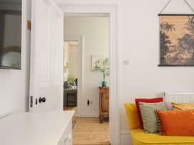 A room with a yellow sofa and colorful cushions a white door opened to reveal a wooden cabinet with a plant and a glimpse of another room with a green sofa at Duncombe Teignmouth