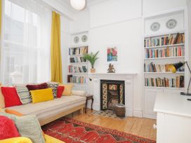 A living room with a sofa with colorful cushions bookshelves fireplace and a red rug at Duncombe in Teignmouth