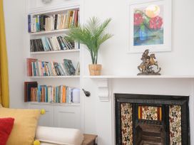 A corner with a built-in bookshelf full of books next to a fireplace with floral tiles and a statue on the mantle at Duncombe in Teignmouth