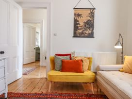 A sitting room with a yellow chair, multi-colored cushions, a beige sofa, a floor lamp, wooden floors, and a wall hanging at Duncombe in Teignmouth