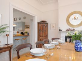 A dining room with a wooden table set with plates glasses and cutlery next to a kitchen with stools and cabinets at Duncombe in Teignmouth