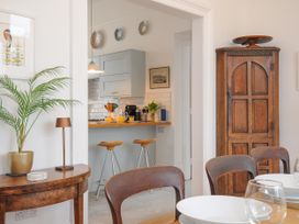 A dining area with wooden chairs and table set with white plates and glasses adjacent to a kitchen with stools and wooden cabinet at Duncombe in Teignmouth