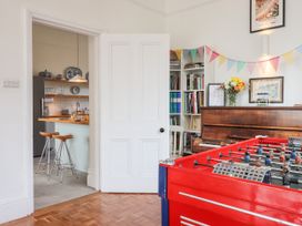 A room with a red foosball table a piano bookshelf and a kitchen with stools and dishes at Duncombe in Teignmouth