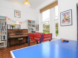 A room with a piano, foosball table, blue ping pong table, shelves with books and two posters on the walls at Duncombe in Teignmouth