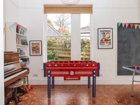 A game room with a red foosball table a piano a bookshelf a window and a ping pong table at Duncombe in Teignmouth