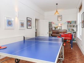 A game room with a ping pong table, foosball table, piano, bookshelves, and framed artwork at Duncombe in Teignmouth