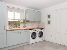 A laundry room with washing machine and dryer under wooden countertop with light blue cabinets and a window at Duncombe in Teignmouth