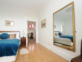 A bedroom with a bed, bedside table, lamp, wall mirror, wooden floor, and open door showing a hallway at Duncombe in Teignmouth