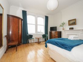 A bedroom with wooden floor two green chairs a wooden table a wardrobe a chest of drawers a bed with blue blanket and window Duncombe Teignmouth