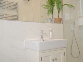 A bathroom sink with a faucet soap dispenser and plant on the countertop with a showerhead on the wall at Duncombe in Teignmouth