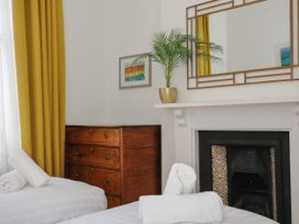 A bedroom with white beds and towels a wooden dresser yellow curtains a plant on a white fireplace and a wall mirror at Duncombe in Teignmouth