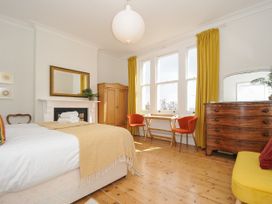 A bedroom with a bed, wooden wardrobe, desk with two orange chairs, wooden chest of drawers with mirror and yellow curtains at Duncombe in Teignmouth