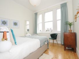 A bedroom with a bed a green chair wooden cabinet and large windows at Duncombe in Teignmouth