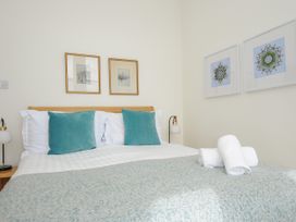 A bedroom with a double bed two teal pillows two white lamps wooden bedside tables and framed pictures on the walls at Duncombe in Teignmouth