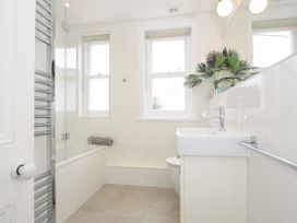 A bathroom with a bathtub with glass screen a sink a toilet two windows and a plant on the sink at Duncombe in Teignmouth