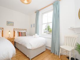 A bedroom with two single beds a wooden floor a window with blue curtains and a white chair at Duncombe in Teignmouth