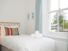 A bedroom with a single bed a striped pillow white towels on the bed and a window with blue curtains at Duncombe in Teignmouth
