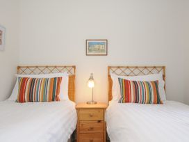 A bedroom with two single beds white bedding colorful striped pillows a wooden nightstand and a lamp at Duncombe in Teignmouth