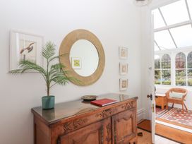 A wooden sideboard with a potted plant, a mirror above and framed pictures on the wall next to a door leading to a sunroom with a wicker chair at Duncombe in Teignmouth
