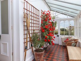 A sunroom with potted plants wooden paddles wicker chairs and a wooden bench at Duncombe in Teignmouth