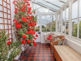 A sunroom with red flowers on a trellis two wicker chairs and a wooden bench at Duncombe in Teignmouth